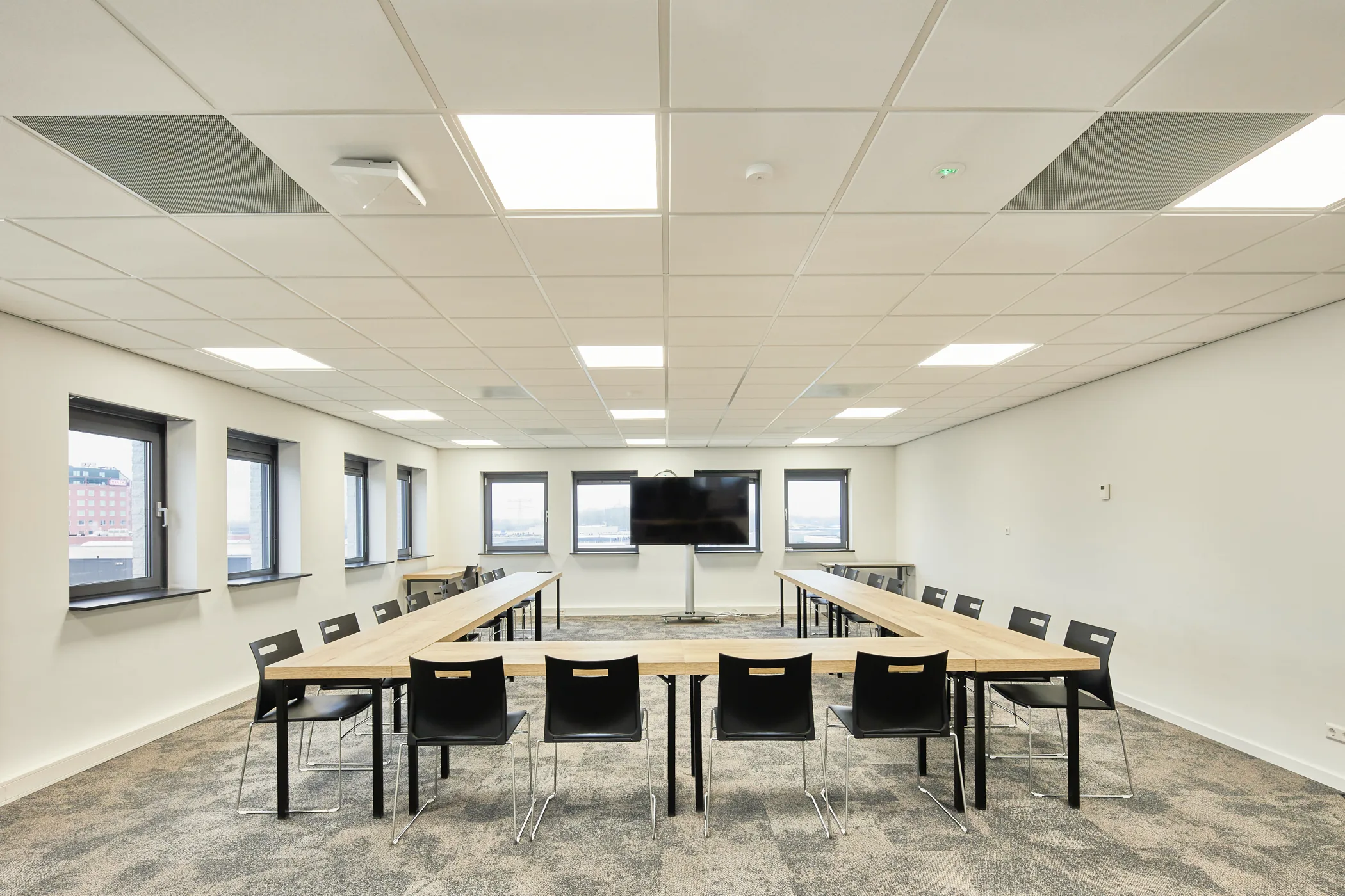 Salle de réunion avec table en U, écran et chaises dans un bâtiment professionnel